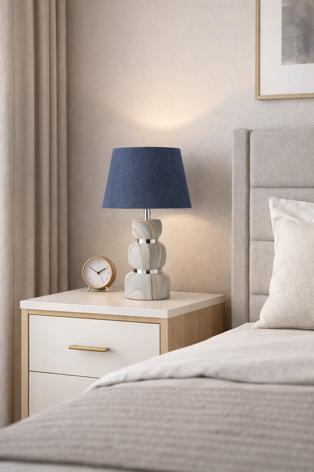 6258b1b2-f7ff-4498-aa88-9bf16b3b7f34 Modern bedside table lamp with blue fabric shade and marble-style base placed on a wooden nightstand next to a bed in a cozy bedroom.