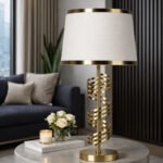 Modern gold spiral table lamp with white fabric shade placed on a round stone coffee table in a luxury living room.